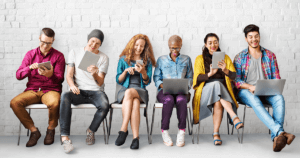 Young-people-on-devices-smiling-sitting-next-to-each-other