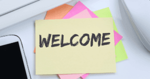 Welcome Written on Top Sticky in Pile in Between Phone and Mouse on Table