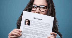 Young Woman with Glasses Holding Resume Up Partially Covering Face on Blue Background