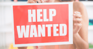 Red Help Wanted Sign Being Put Up in Window of Retail Store (1)