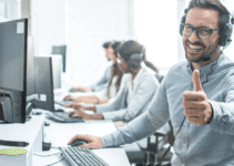 Man with Glasses Wearing Headset in Front of Computer Smiling and Giving Thumbs Up