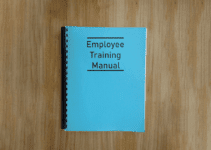Blue Bound Book with Employee Training Manual on Cover Sitting on Light Wood Desk