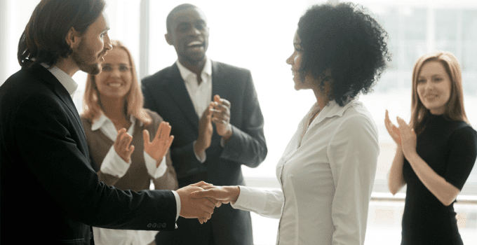 Group of Businesspeople Clapping in Congratulations for Young Woman Shaking Boss's Hand