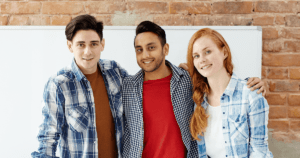 Three Young People Arm-In-Arm in Office Workroom in Front of Whiteboard