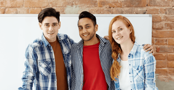 Three Young People Arm-In-Arm in Office Workroom in Front of Whiteboard