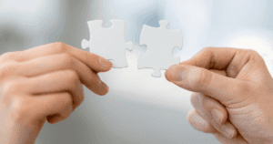 Man and Woman's Hands Holding White Jigsaw Puzzle Pieces Together
