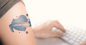 How 4 Major Companies are Retaining Employees - Person Typing at Keyboard with Closeup of I Love My Company Tattoo on Arm